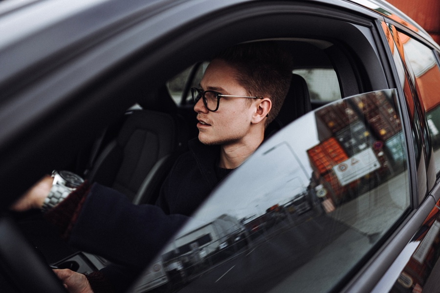 Junger Mann mit Brille sitzt in einem modernen Auto und schaut konzentriert aus dem Fenster – Symbolbild für Restwert Leasing und kalkulierte Fahrzeugnutzung.