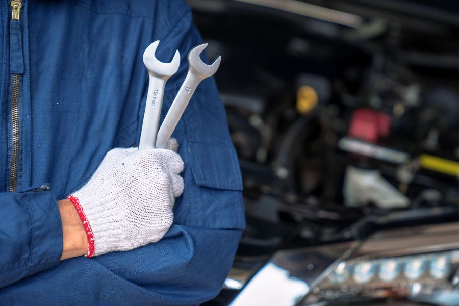 A man with wrenches stands in front of a car under repair. A symbol for maintenance and repair.
