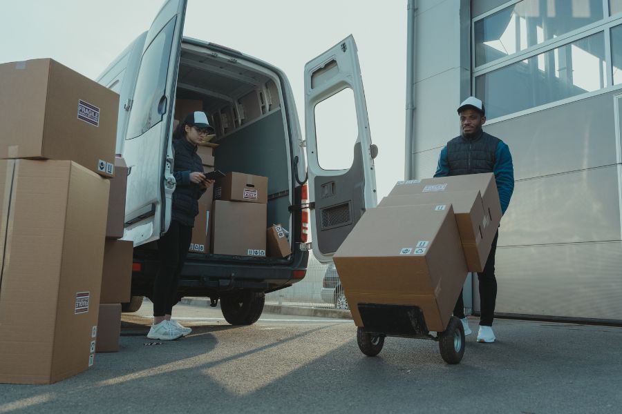 Two employees unload a delivery van with boxes after a company trip.
