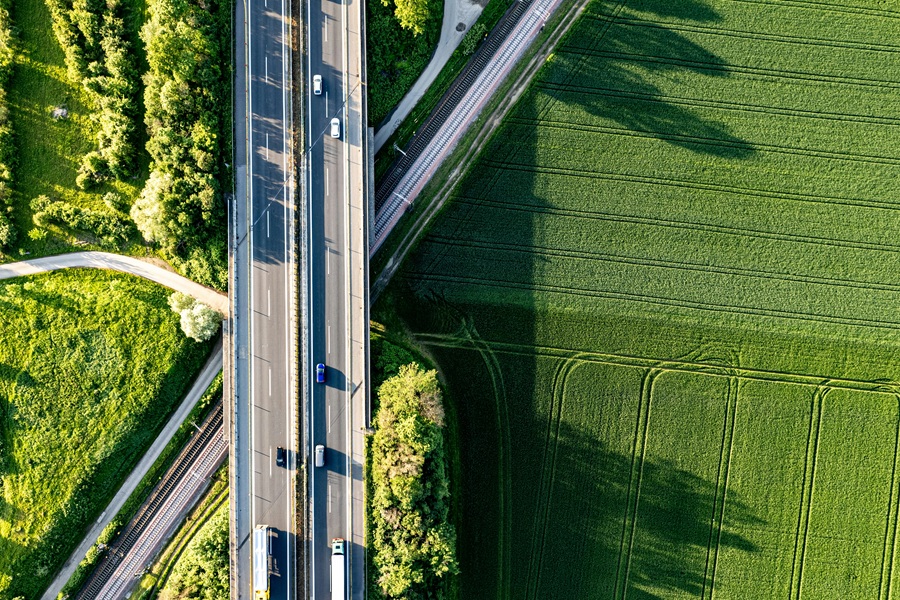 Aerial view of a highway bridge with cars and trucks over green fields and railroad tracks, symbol for sustainable mobility and GHG quota in road traffic