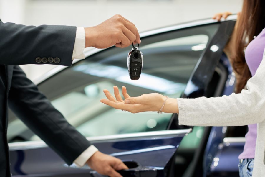 An employee hands a woman a car key. A symbolic image for car owners.