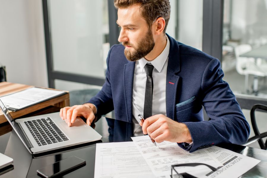 A man sits at his desk and works on his laptop. A symbolic image for the vehicle owner.