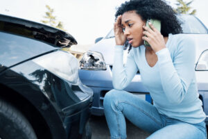 A stressed driver talks on the phone in front of two damaged cars. The scene shows the effort involved in accidents. Claims management software facilitates digital reporting and documentation. Fleet+ offers integrated claims management, bundles images, appraisals and invoices centrally and enables efficient analysis of key areas of damage.