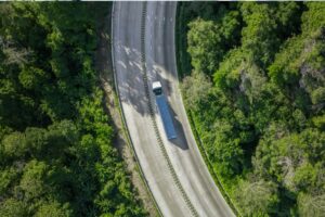 Luftaufnahme eines Lkw auf einer kurvigen Straße durch dichten Wald. Das Bild steht für nachhaltiges Fuhrparkmanagement mit Fokus auf digitale Mobilitätslösungen von Carano, effiziente Flottenprozesse, CO2 Reduktion, Compliance, Transparenz und wirtschaftliche Optimierung von Unternehmensfuhrparks.