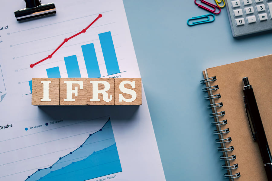 The abbreviation "IFRS" is written in wooden letters on an annual report with diagrams. The illustration refers to international accounting standards that define the requirements for the accounting of assets and leasing contracts and thus also create financial transparency in fleet management.